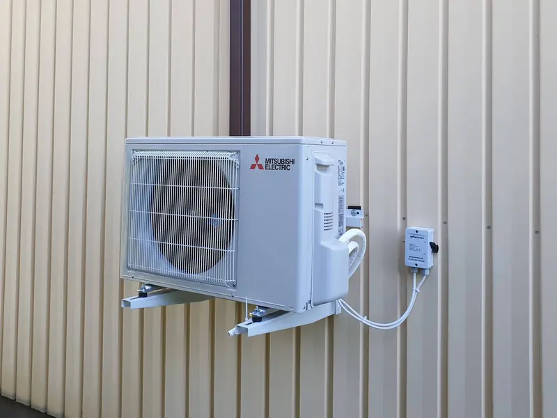 Mitsubishi Electric -ilmalämpöpumpun ulkoyksikkö seinätelineellä vaalealla peltiseinällä